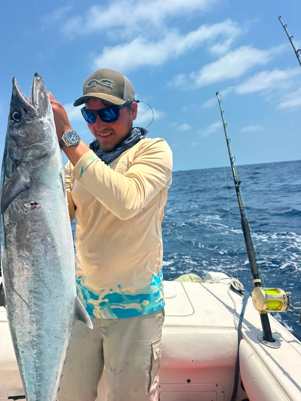 Angler holding a kingfish beside the rod that caught it