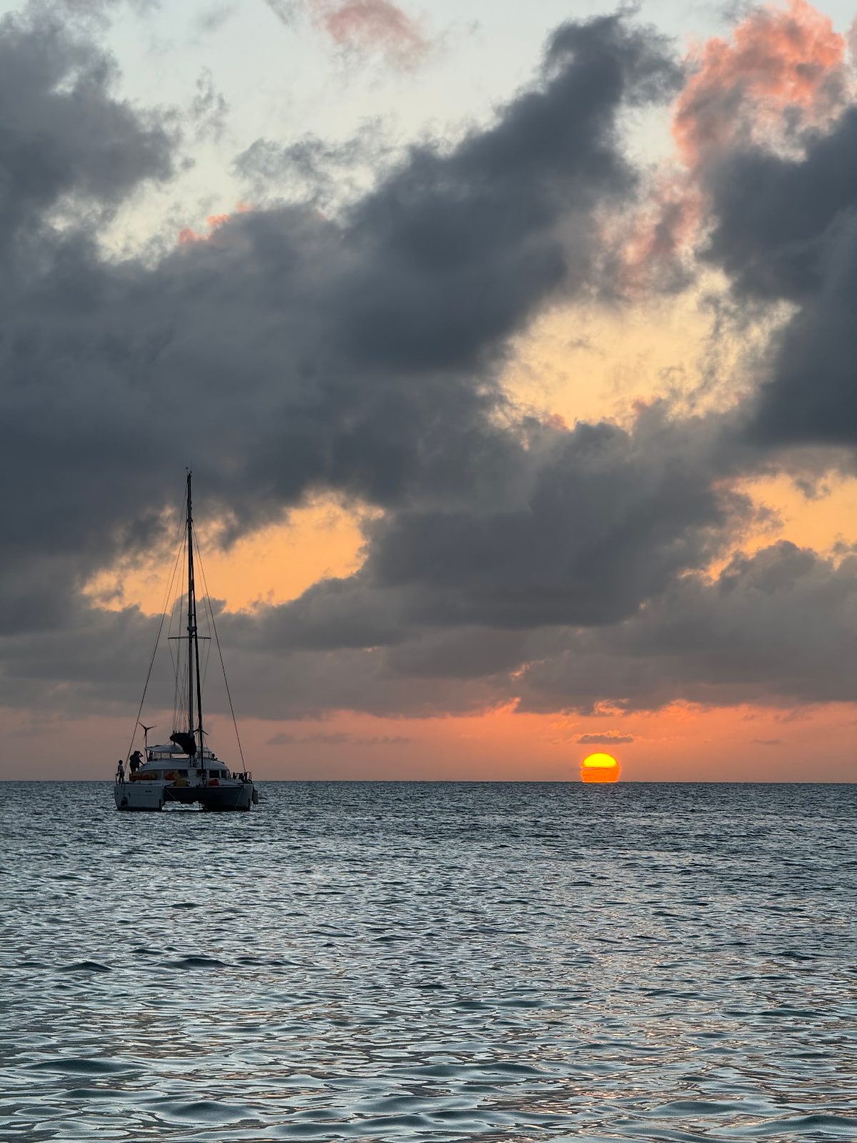 A catamaran silhouetted against a Belize sunset on calm water